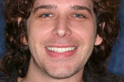 Full-face after smile makeover photo of a male patient with curly, shoulder-length brown hair and blue eyes; from the office of Baton Rouge dentist Dr. Brooksher.